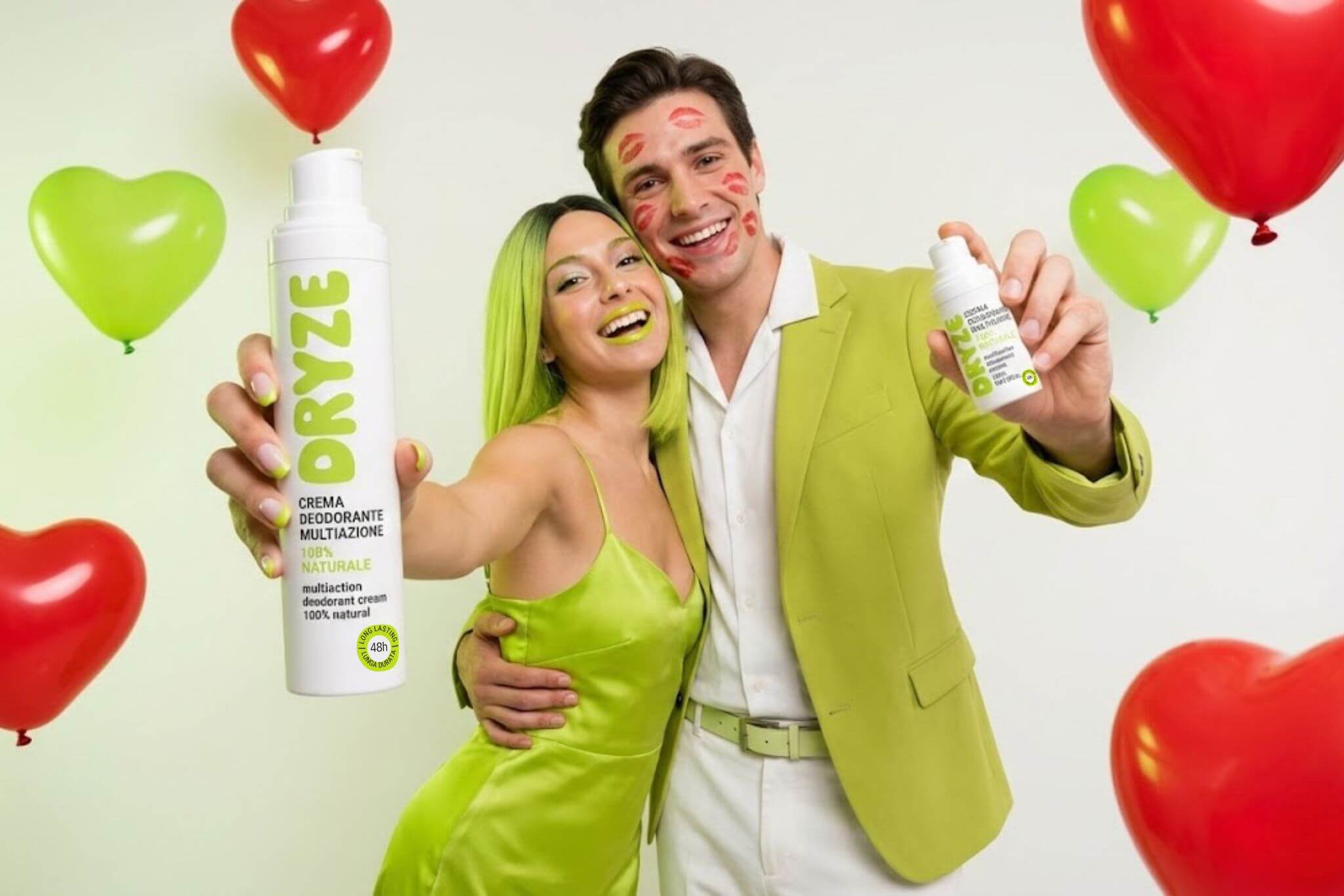 Uomo e donna sorridenti immersi in palloncini a forma di cuore per la promo di San Valentino, tengono in mano i deodoranti crema DRYZE come idea regalo.