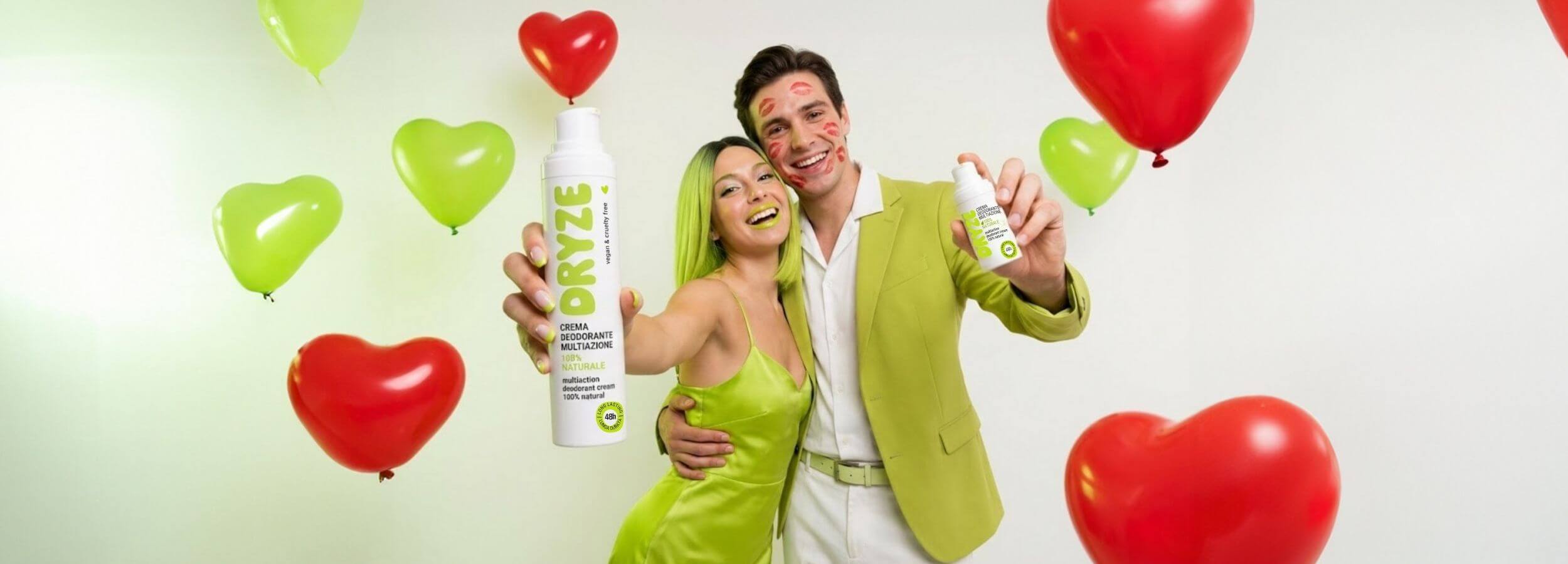 Coppia che festeggia San Valentino con palloncini a cuore rossi e verdi, entrambi mostrano il deodorante crema naturale DRYZE. L'uomo ha stampe di rossetto sul viso.